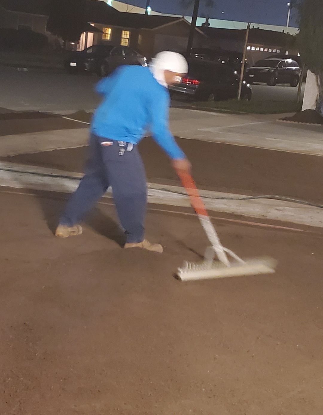 A worker raking a large area of bare soil level in the evening