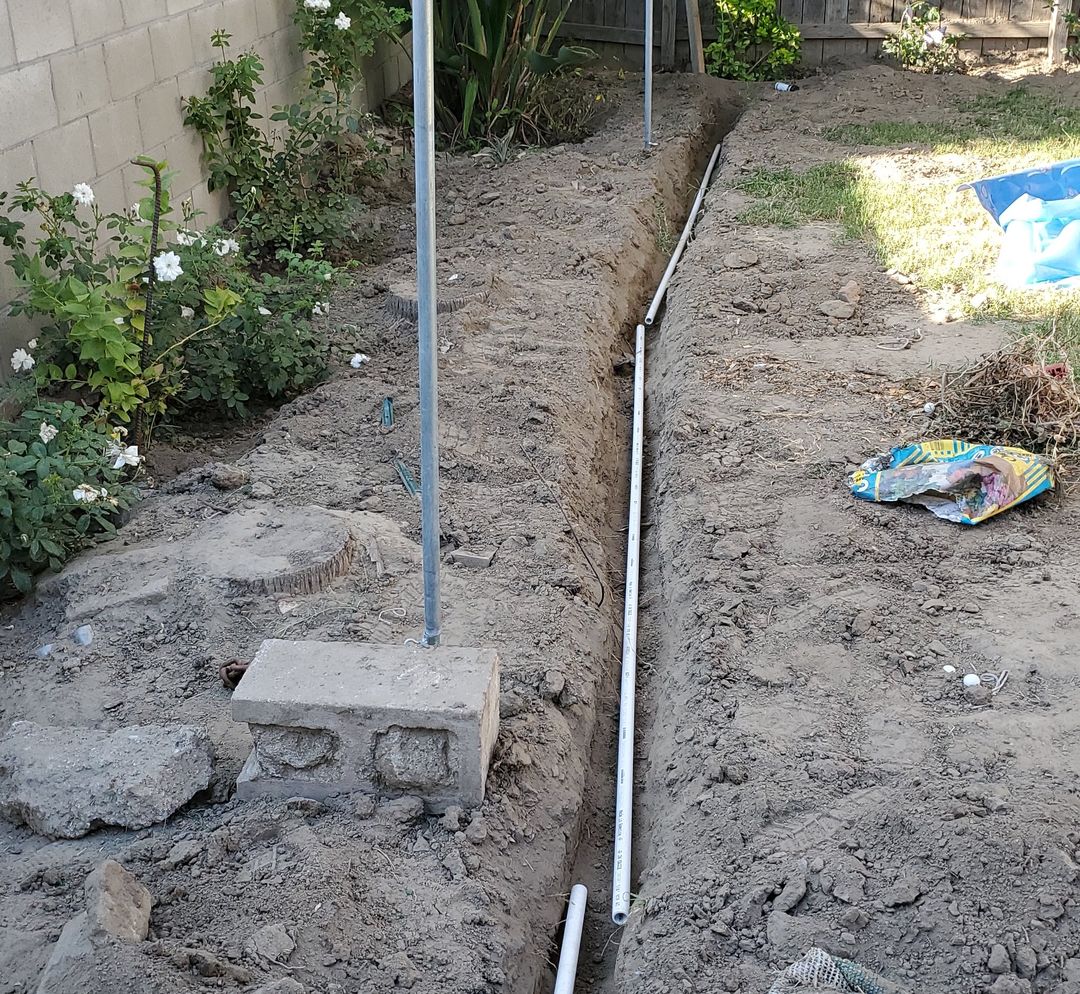 Open trench in a garden bed with new PVC irrigation pipe laid in it