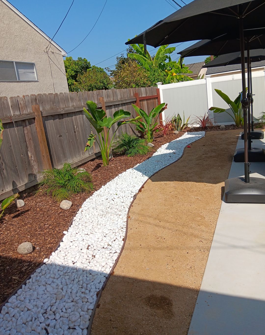 Side yard with a white river-rock bed, a decomposed granite path and new planting along the fence